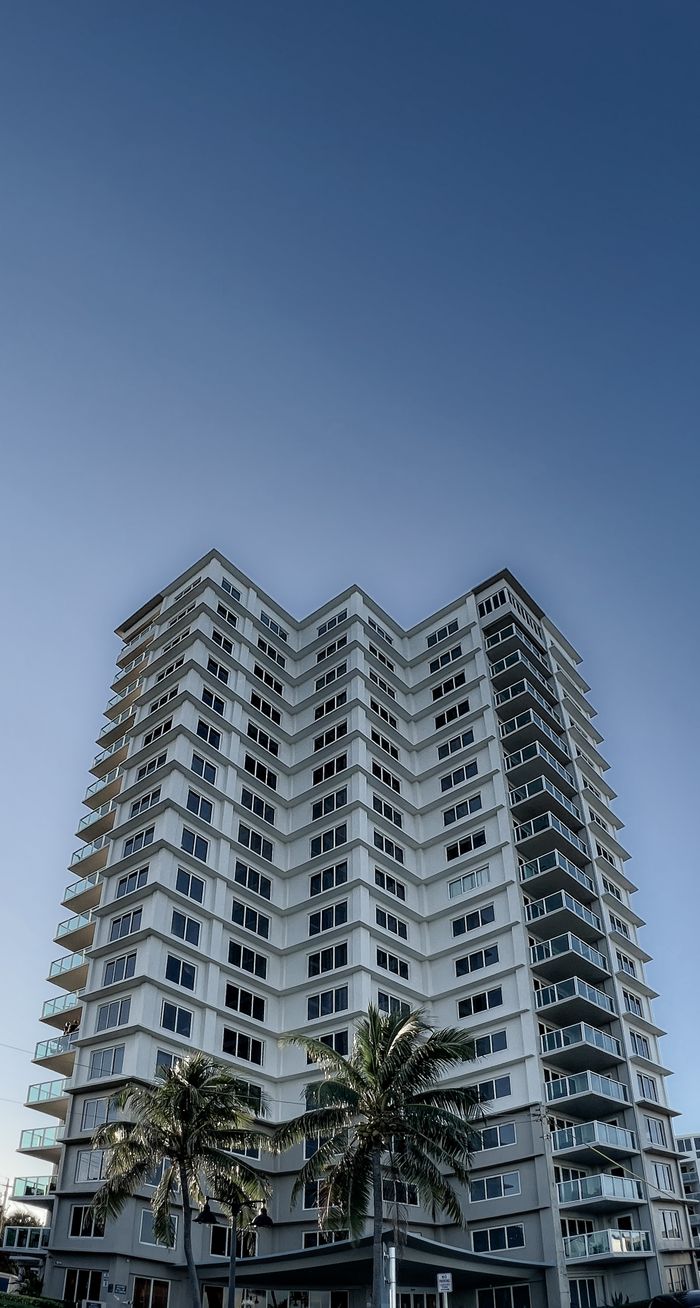 Low-angle view of a tall condominium building under a clear blue sky.